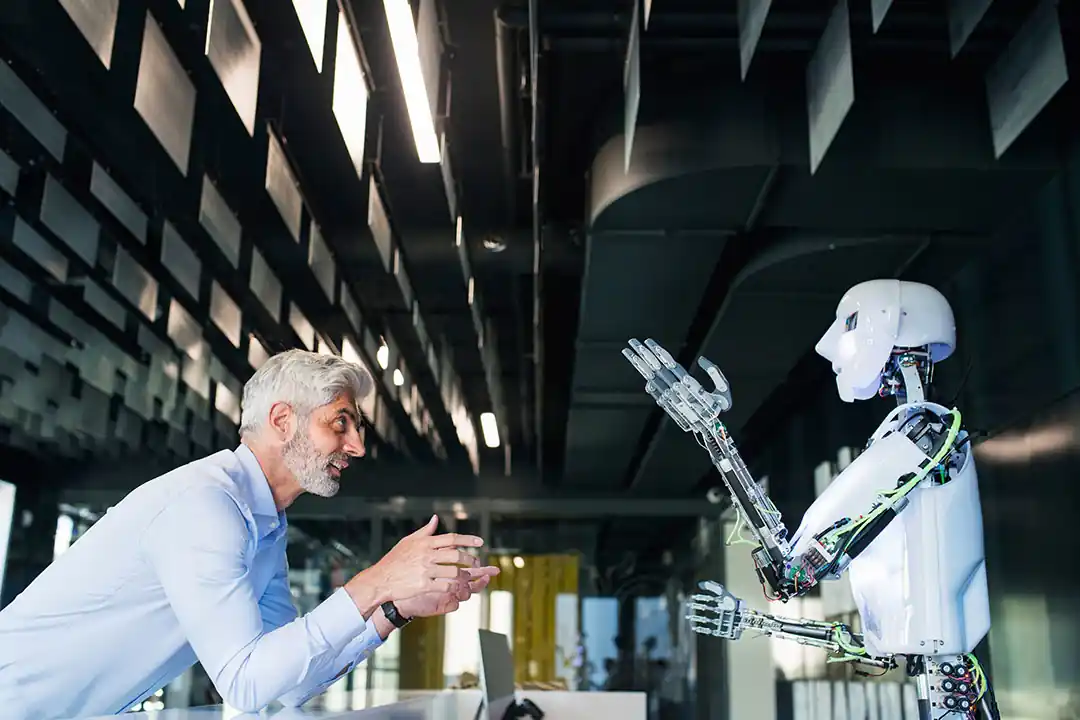 Smiling engineer interacting with a humanoid robot in a modern industrial setting, symbolizing human-AI collaboration within the Internet of Things ecosystem.